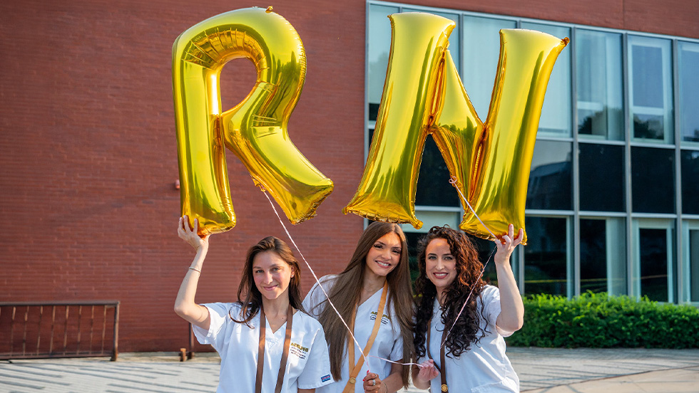 Three female nursing students in scrubs holding R and N balloons 