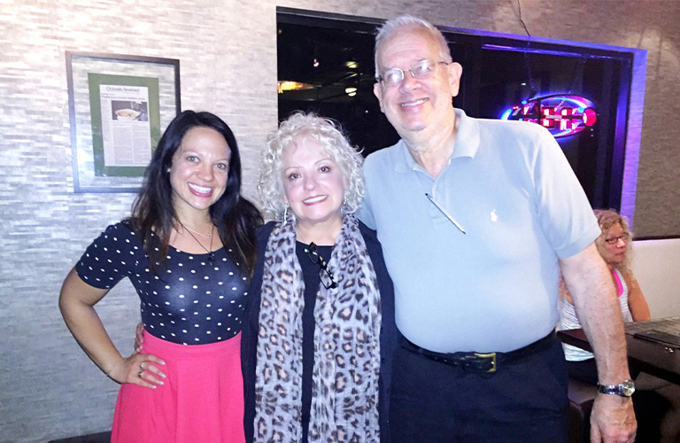 A smiling family of a young daughter on the left, mother with long scarf in the middle, and a tall man, Larry Cohen, on the right.
