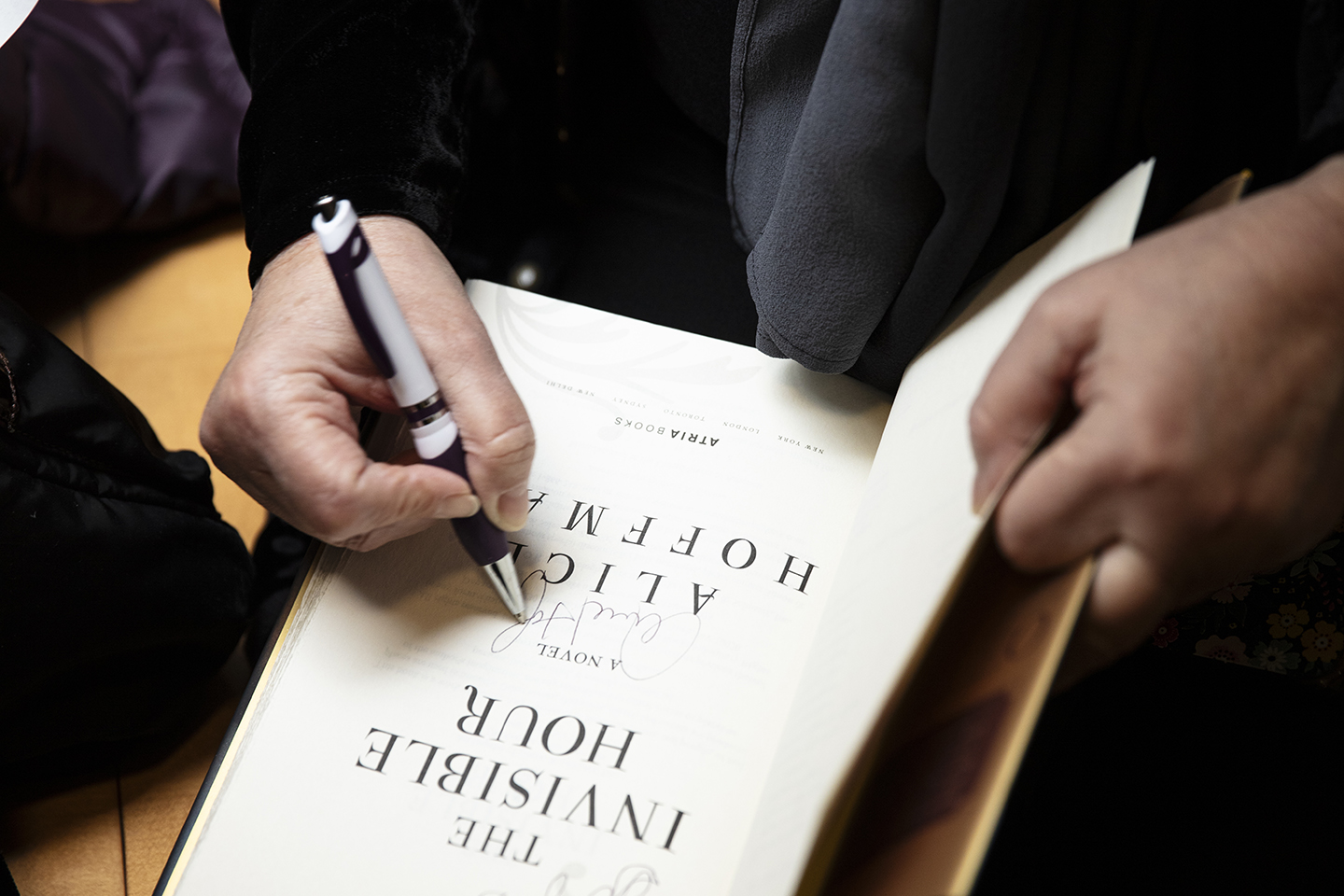 A close-up of Hoffman’s book The Invisible Hour. You only see the author’s hands as she signs the title page of the novel.