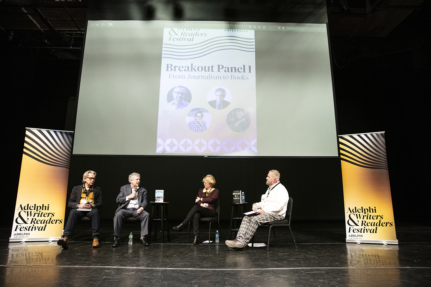The four panelists on stage and in conversation. A screen behind them announces the name of the event: Breakout Panel 1: From Journalism to Books. The screen also has small headshots of each of the writers.